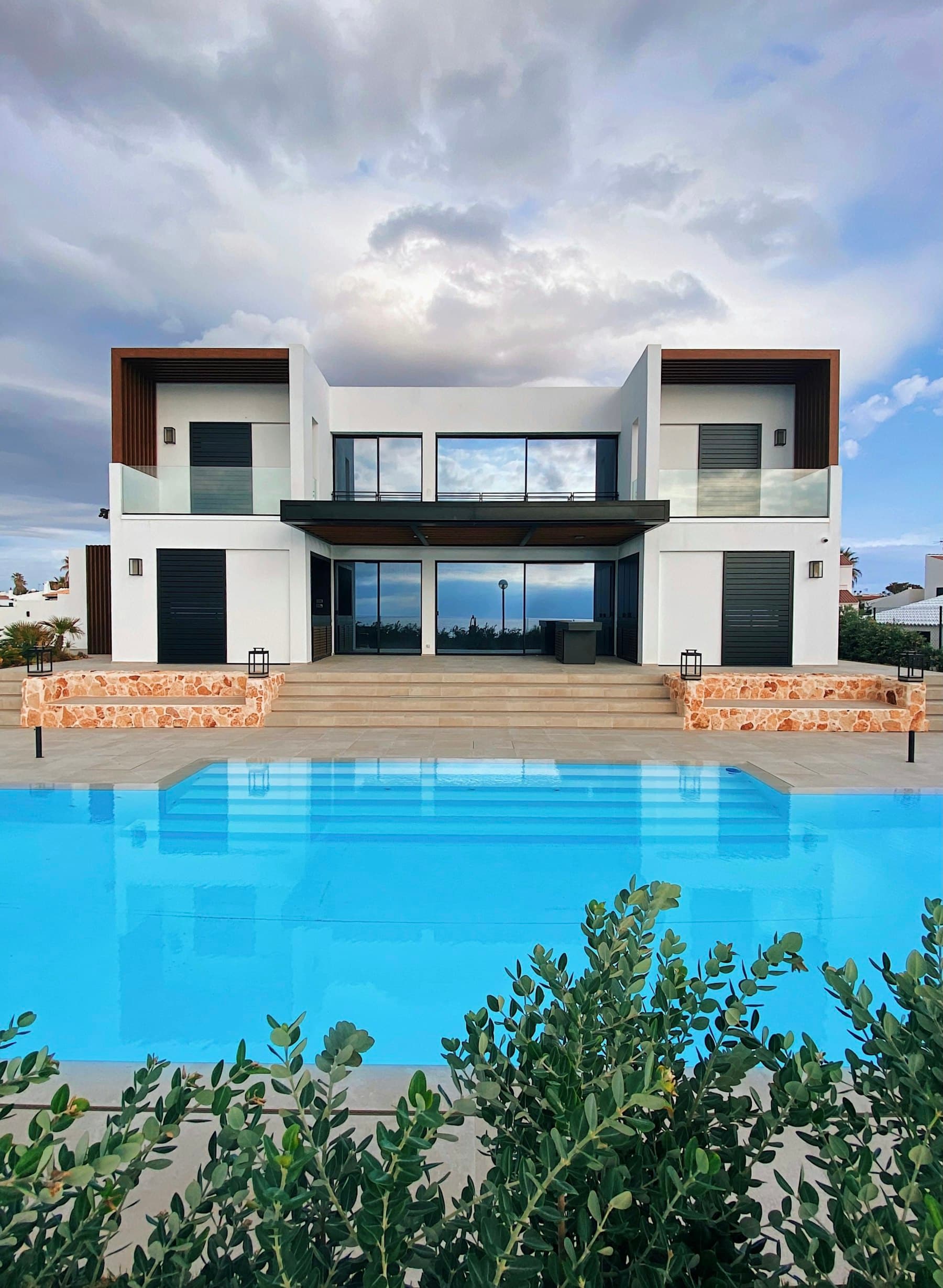 White contemporary villa with a still pool and olive in the foreground.
