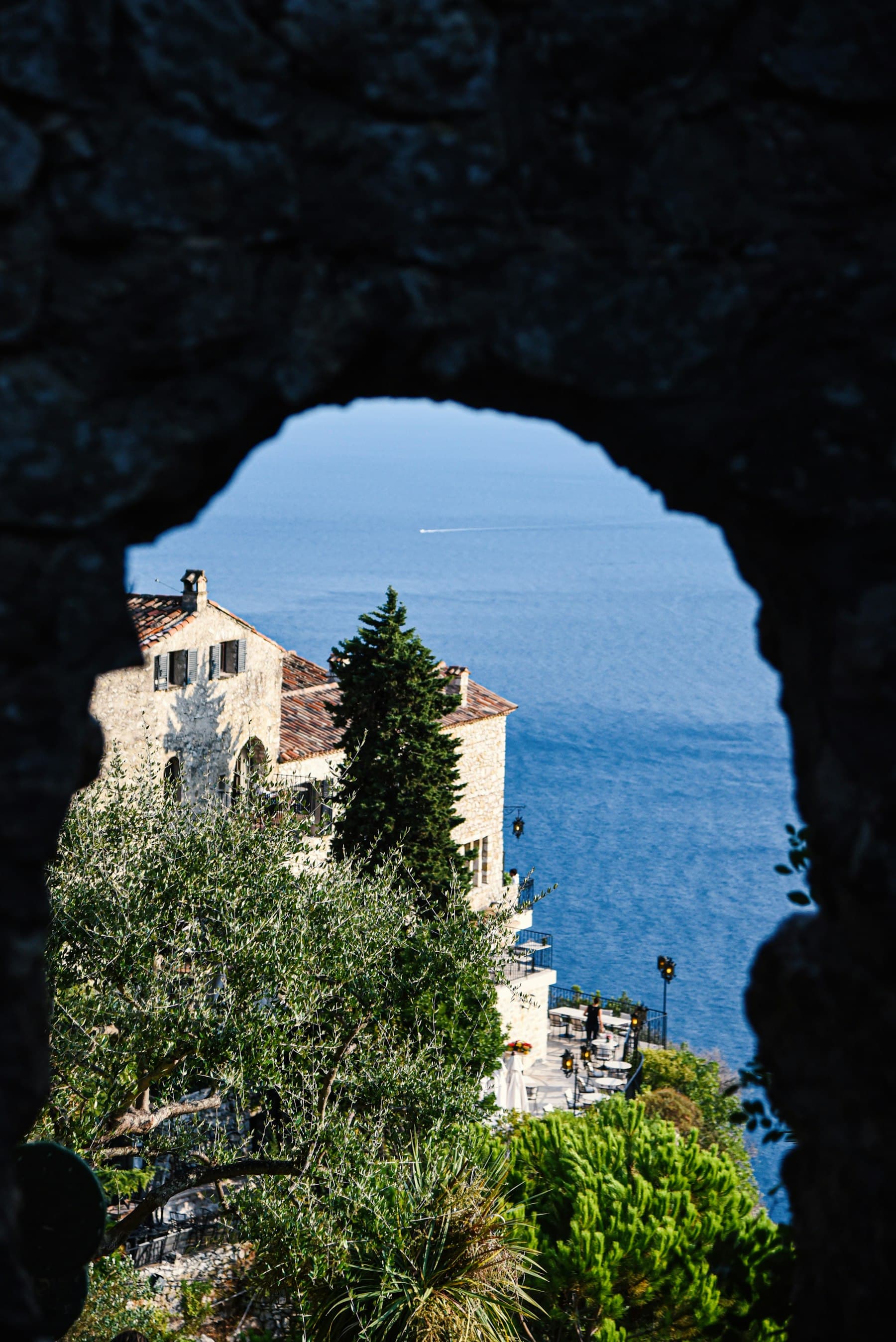A stone arch framing the sea beyond a coastal house.